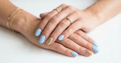 Hands with baby blue nail polish and gold glitter accent nails in a professional beauty photography style