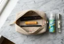 Travel toiletry bag with essential makeup items including mascara, lip balm, eyeliner, dry shampoo and roll-on perfume