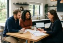Young couple reviewing home loan documents with mortgage advisor at modern kitchen table